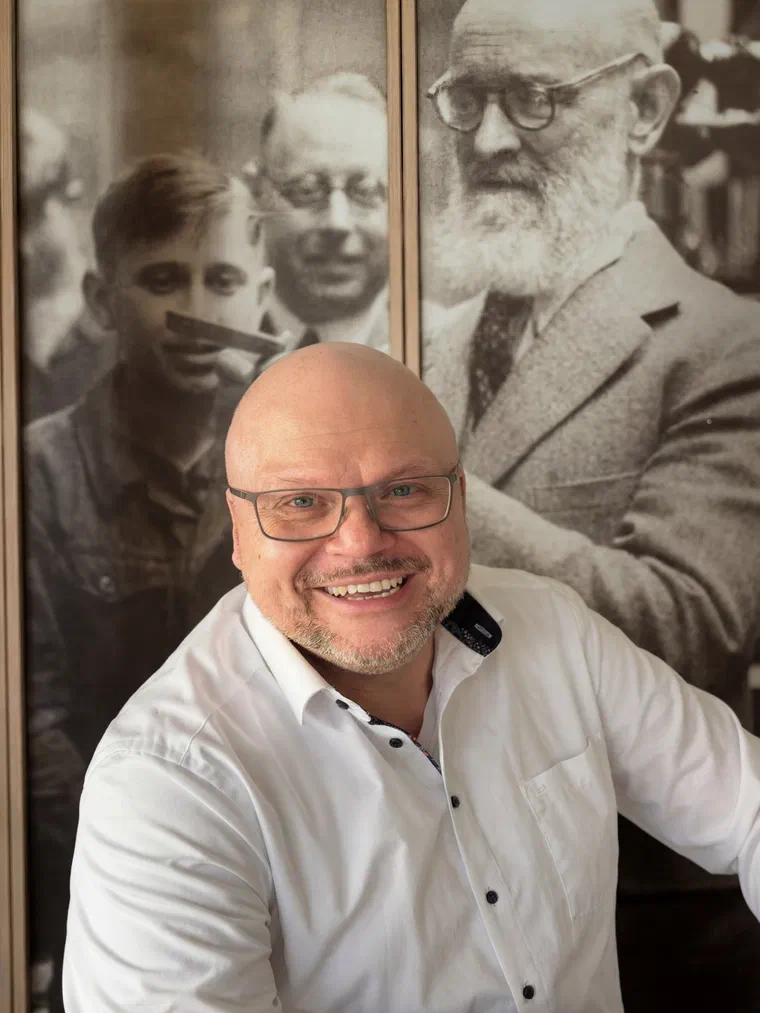 John Loschnig, smiling, in a white shirt, in front of a large sepia photograph of Robert Bosch